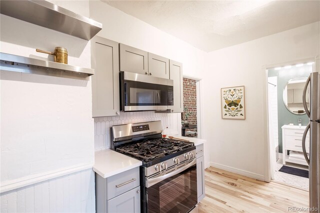 kitchen with appliances with stainless steel finishes, gray cabinets, light wood-style flooring, light countertops, and tasteful backsplash