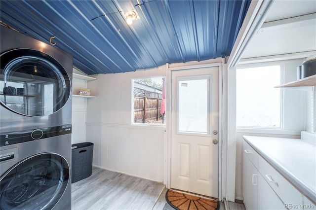 laundry room featuring stacked washer / dryer, light wood finished floors, and wooden ceiling
