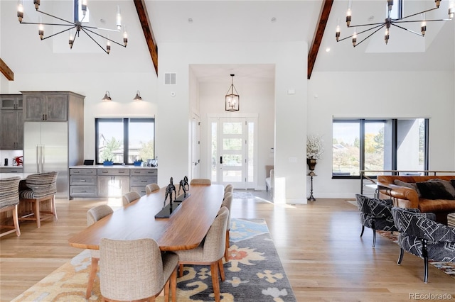 dining room with a chandelier, light hardwood / wood-style flooring, beamed ceiling, and a high ceiling