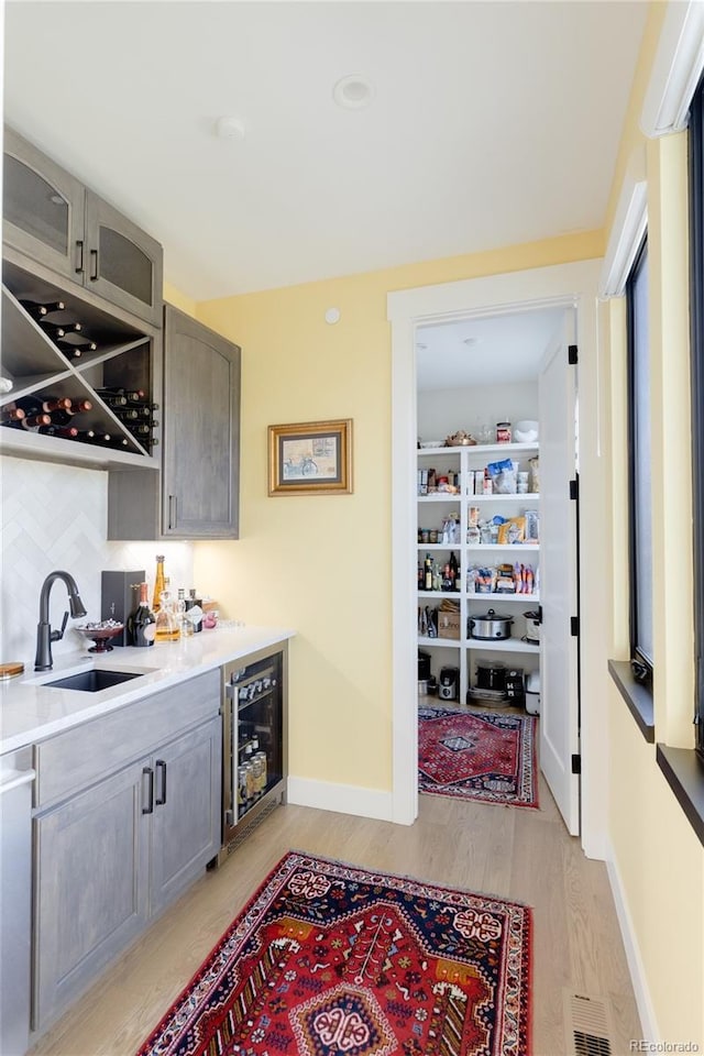 bar with dishwashing machine, wine cooler, decorative backsplash, sink, and light wood-type flooring