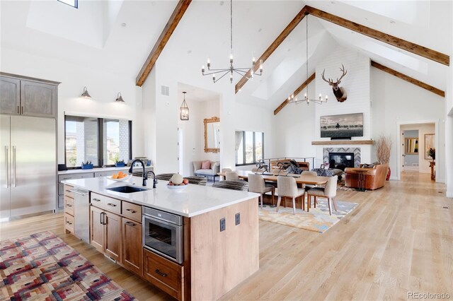 kitchen with sink, a center island with sink, built in appliances, and high vaulted ceiling