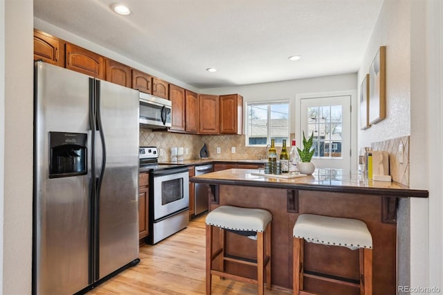 2285 Fulton St, Aurora, CO 80010 - kitchen with stainless steel appliances, a peninsula, backsplash, a breakfast bar area, and light wood-style flooring