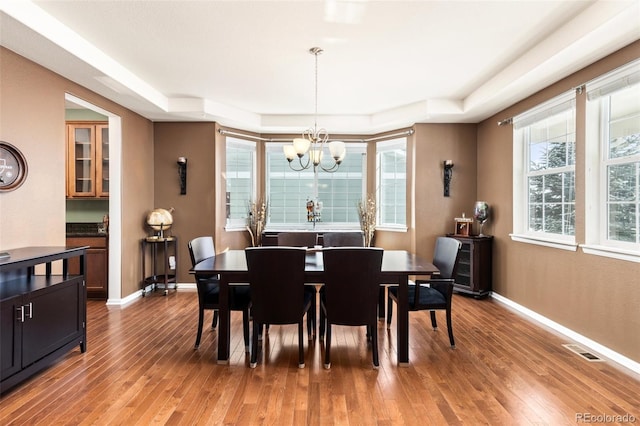 dining space featuring light hardwood / wood-style flooring, a raised ceiling, and a chandelier