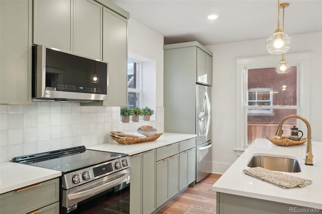 kitchen with appliances with stainless steel finishes, hanging light fixtures, light wood-type flooring, sink, and tasteful backsplash