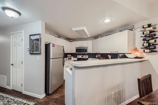 kitchen with white cabinetry, dark hardwood / wood-style floors, kitchen peninsula, and appliances with stainless steel finishes