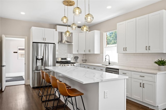 kitchen featuring wall chimney exhaust hood, white cabinets, tasteful backsplash, a kitchen island, and appliances with stainless steel finishes