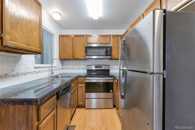 kitchen with stainless steel appliances, sink, backsplash, and light hardwood / wood-style flooring