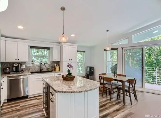 kitchen featuring a kitchen island, decorative backsplash, stainless steel dishwasher, white cabinetry, and a sink