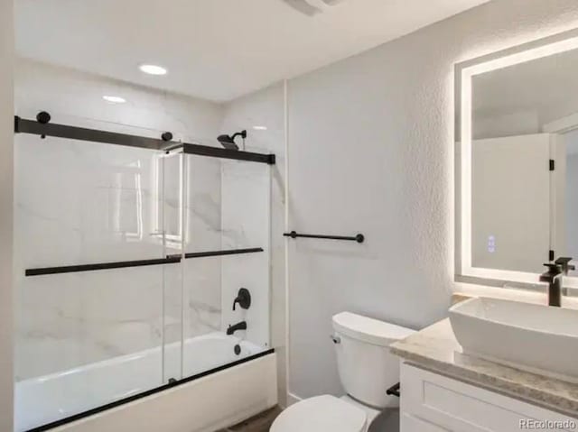 full bathroom with vanity, toilet, a textured wall, and combined bath / shower with glass door