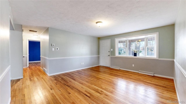 empty room with a textured ceiling and light hardwood / wood-style flooring