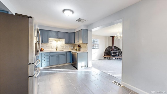 kitchen with a wood stove, backsplash, sink, stainless steel appliances, and a chandelier