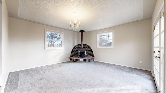 carpeted empty room featuring a raised ceiling, a wood stove, a chandelier, and a textured ceiling