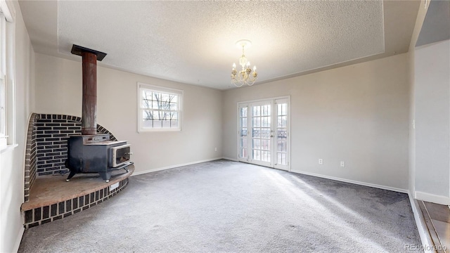 unfurnished living room featuring a wood stove, dark carpet, a textured ceiling, and a notable chandelier