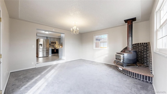 unfurnished living room featuring dark carpet, a textured ceiling, an inviting chandelier, and a wood stove