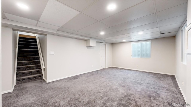 basement featuring a paneled ceiling and dark carpet