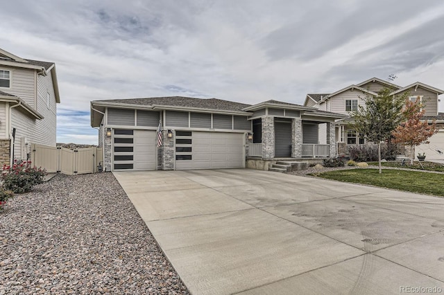 view of front of house with driveway, stone siding, an attached garage, a gate, and a porch