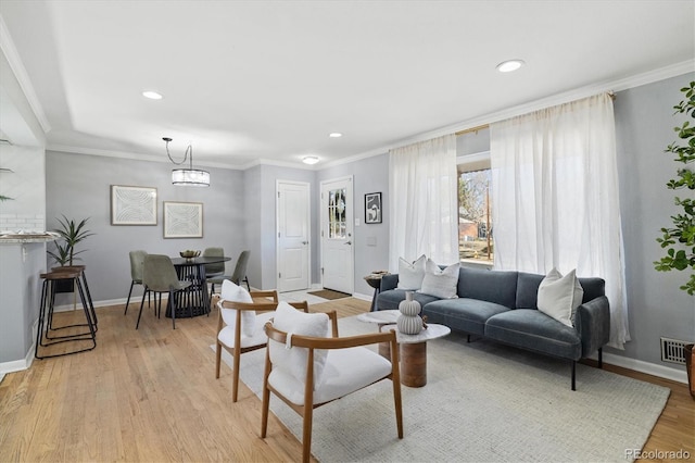 living area featuring light wood finished floors, baseboards, visible vents, and ornamental molding