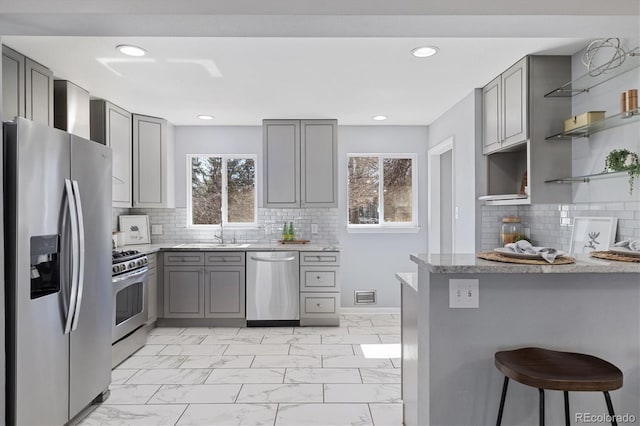 kitchen featuring light stone counters, marble finish floor, open shelves, gray cabinetry, and appliances with stainless steel finishes