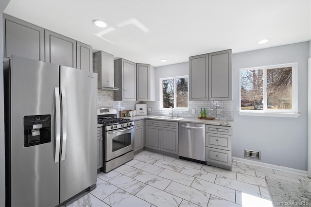 kitchen featuring gray cabinetry, stainless steel appliances, a sink, marble finish floor, and wall chimney range hood