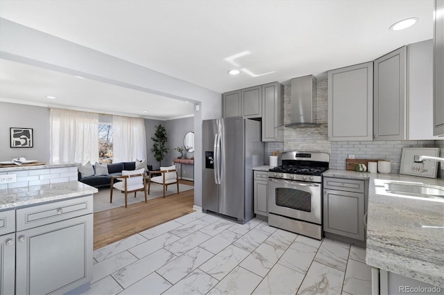 kitchen featuring wall chimney range hood, appliances with stainless steel finishes, gray cabinets, and a sink