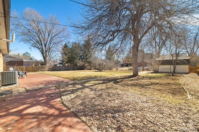 view of yard with central AC unit, a fenced backyard, an outdoor structure, a patio area, and a shed