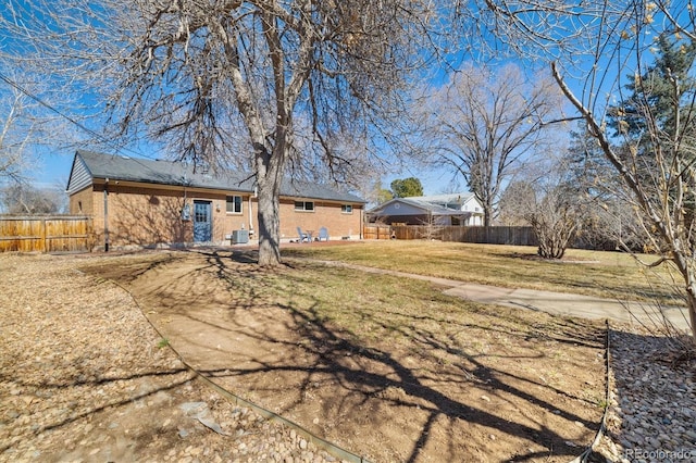 back of house featuring brick siding, fence, and a lawn