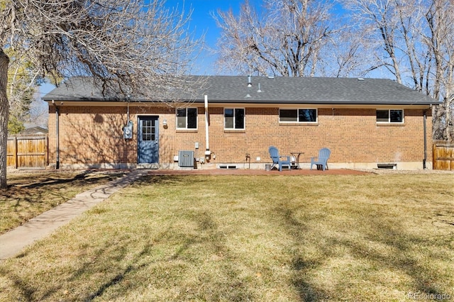 back of property featuring brick siding, a shingled roof, a lawn, central AC unit, and fence