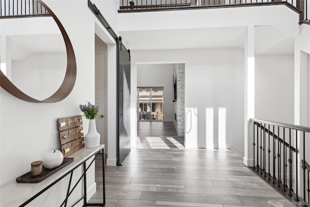 corridor with a barn door, wood finished floors, a towering ceiling, and baseboards