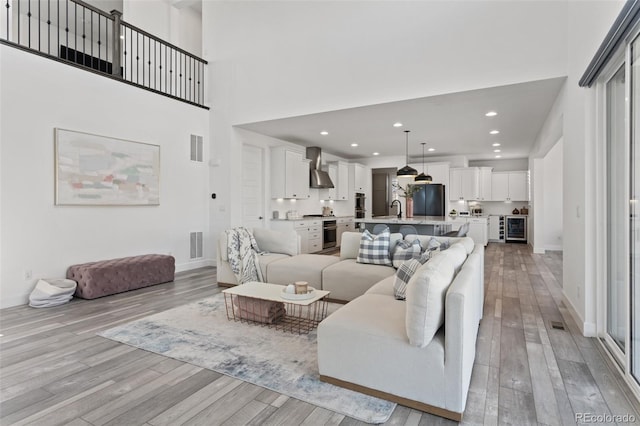 living room with light wood-style floors, visible vents, and a towering ceiling