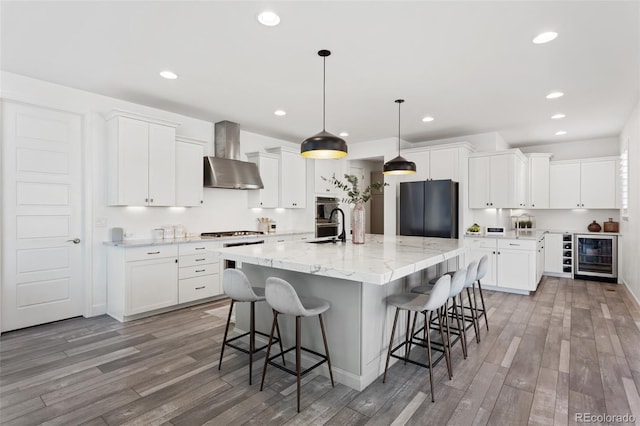 kitchen featuring wine cooler, freestanding refrigerator, a sink, wall chimney range hood, and light wood-type flooring