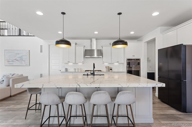 kitchen with wall chimney range hood, a kitchen bar, white cabinetry, and stainless steel appliances