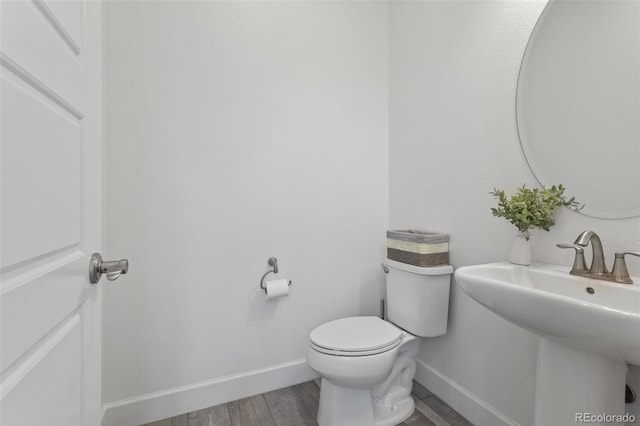 bathroom featuring toilet, a sink, baseboards, and wood finished floors