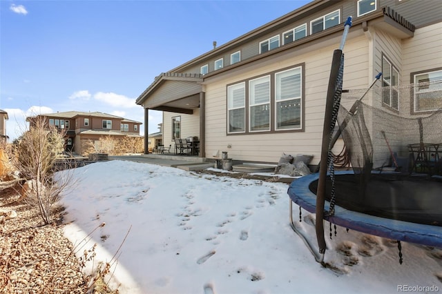 snow covered back of property with a patio area and a trampoline