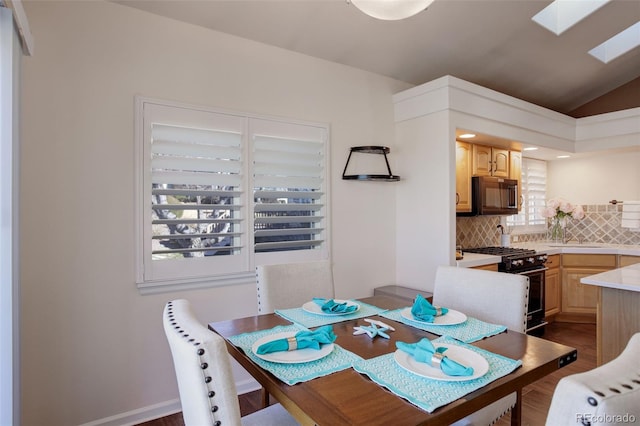 dining area featuring vaulted ceiling with skylight and dark wood finished floors