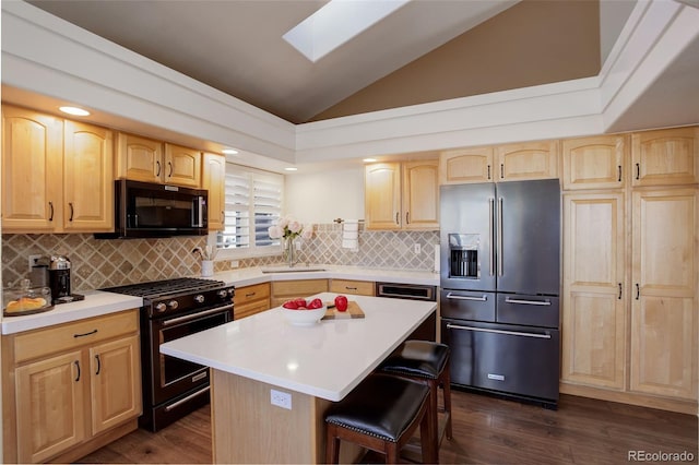 kitchen with a breakfast bar, light countertops, light brown cabinetry, vaulted ceiling with skylight, and black appliances