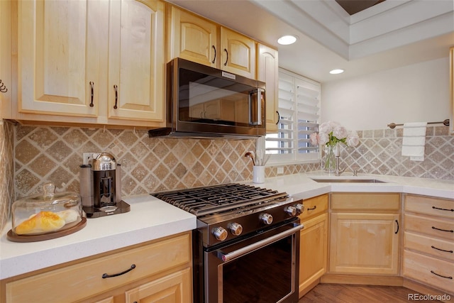 kitchen featuring stainless steel gas range, light countertops, a sink, and light brown cabinetry