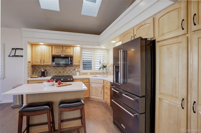 kitchen with range with gas cooktop, high quality fridge, a kitchen breakfast bar, light brown cabinetry, and a sink