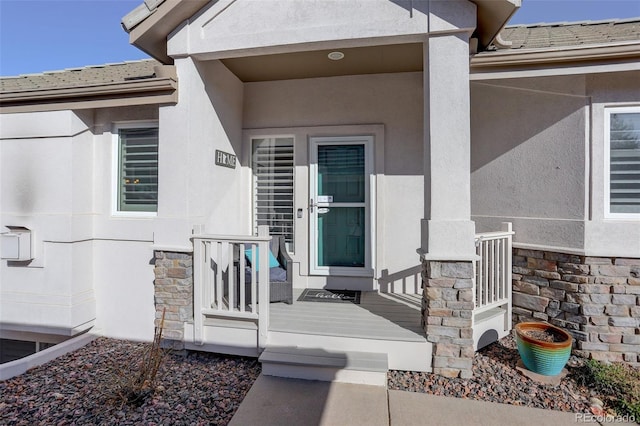 property entrance with stone siding, a porch, roof with shingles, and stucco siding