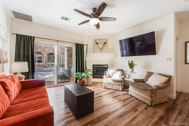 living room featuring a ceiling fan, a glass covered fireplace, visible vents, and wood finished floors