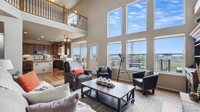 11818 Rio Secco Rd, Peyton, CO 80831 - living room featuring plenty of natural light, light wood finished floors, a towering ceiling, a chandelier, and baseboards