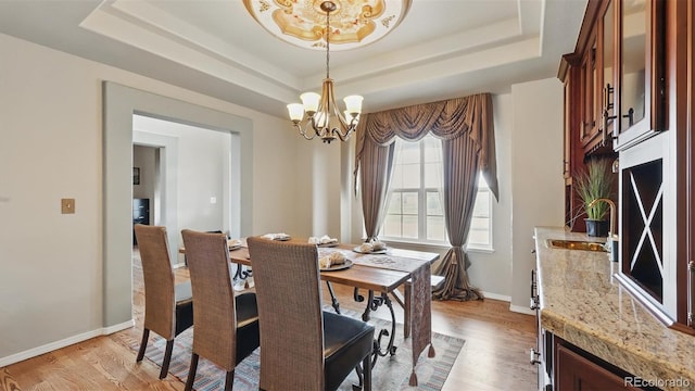 11818 Rio Secco Rd, Peyton, CO 80831 - dining area featuring a chandelier, a tray ceiling, light wood-style floors, and baseboards