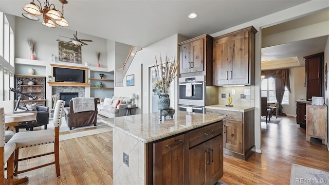 11818 Rio Secco Rd, Peyton, CO 80831 - kitchen with light wood-style flooring, double oven, a fireplace, ceiling fan, and light stone countertops