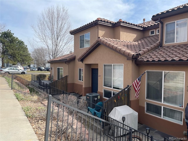 exterior space with central AC unit, a tiled roof, fence, and stucco siding