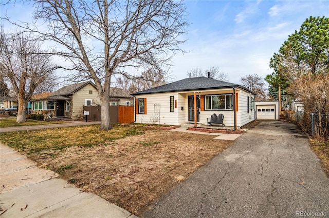 bungalow featuring aphalt driveway, fence, an outbuilding, and a shingled roof