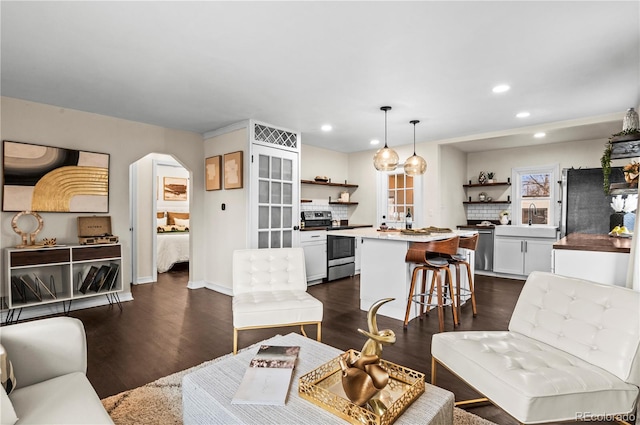 living area featuring arched walkways, recessed lighting, dark wood-type flooring, and baseboards