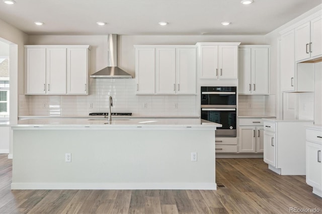 kitchen featuring white cabinetry, an island with sink, and wall chimney range hood