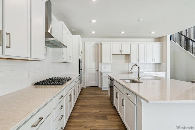 kitchen with sink, white cabinets, a kitchen island with sink, stainless steel appliances, and wall chimney range hood