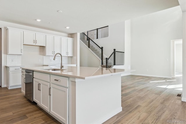 kitchen with white cabinetry, sink, an island with sink, and light wood-type flooring