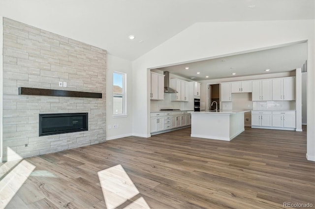 kitchen with a kitchen island with sink, wall chimney range hood, white cabinetry, and tasteful backsplash