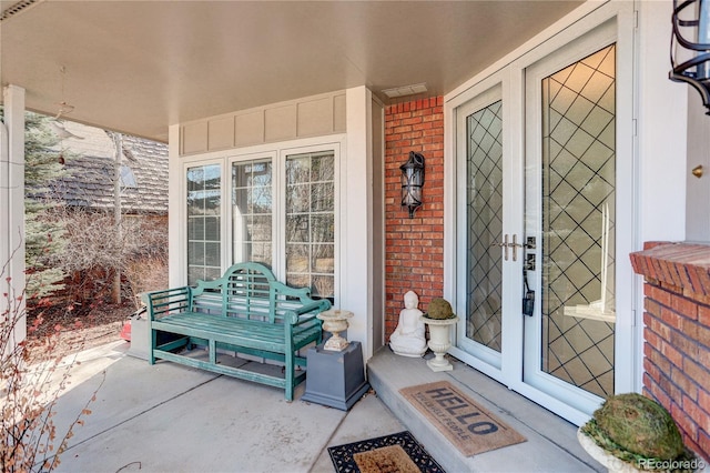 entrance to property featuring covered porch, french doors, brick siding, and visible vents